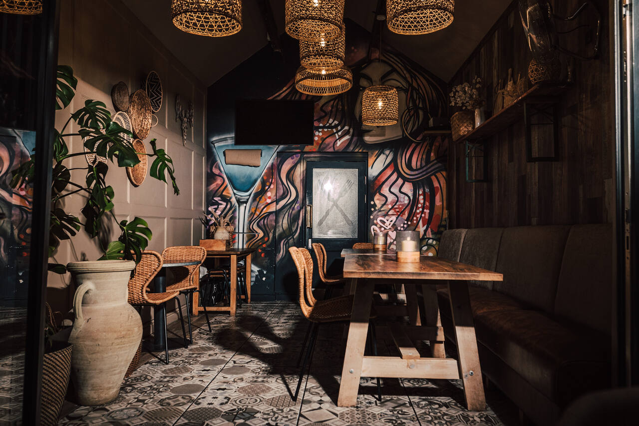 Warmly lit seating area at No.3a with tables, woven pendant lights and a colourful mural